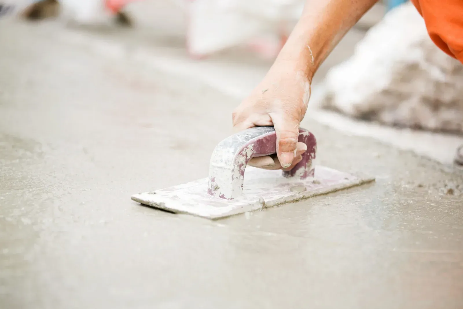 A person is using a trowel to spread concrete on the ground.