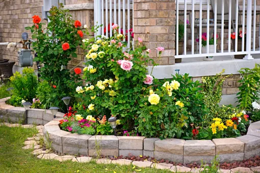 A garden with flowers and plants in front of a brick house.