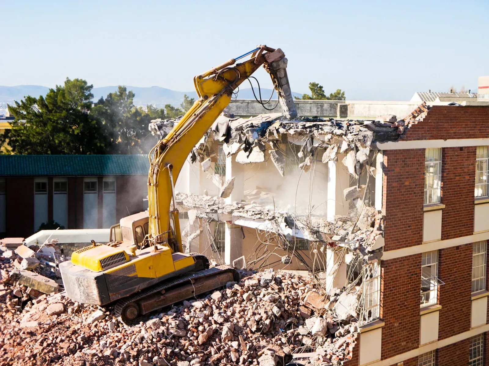 A yellow excavator is demolishing a brick building.