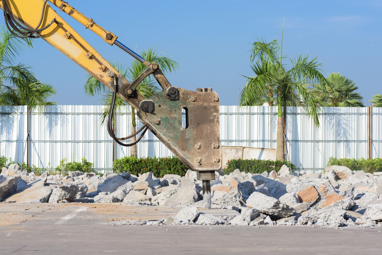 A yellow excavator is breaking concrete on a construction site.