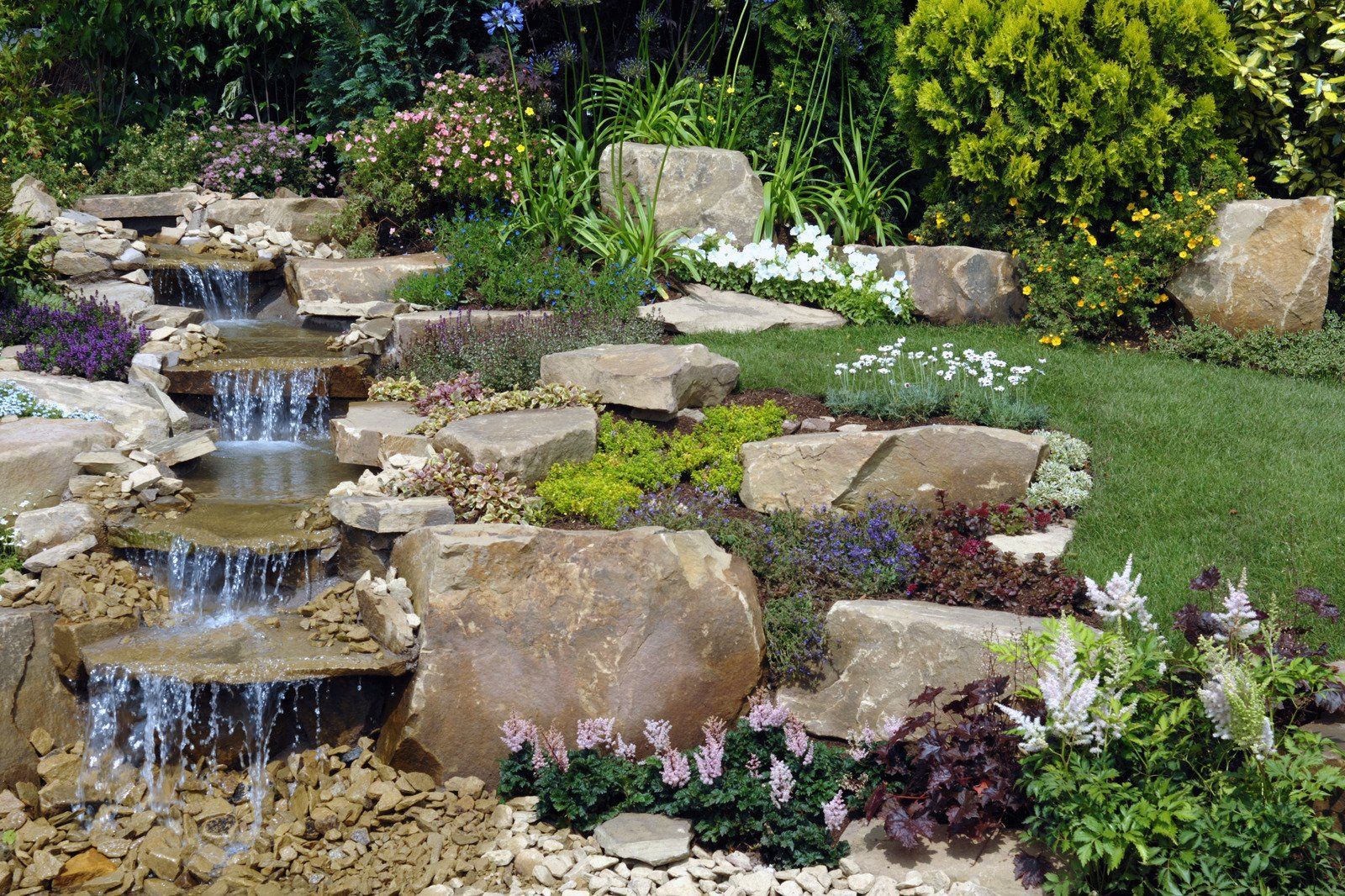 A waterfall is surrounded by rocks and flowers in a garden.