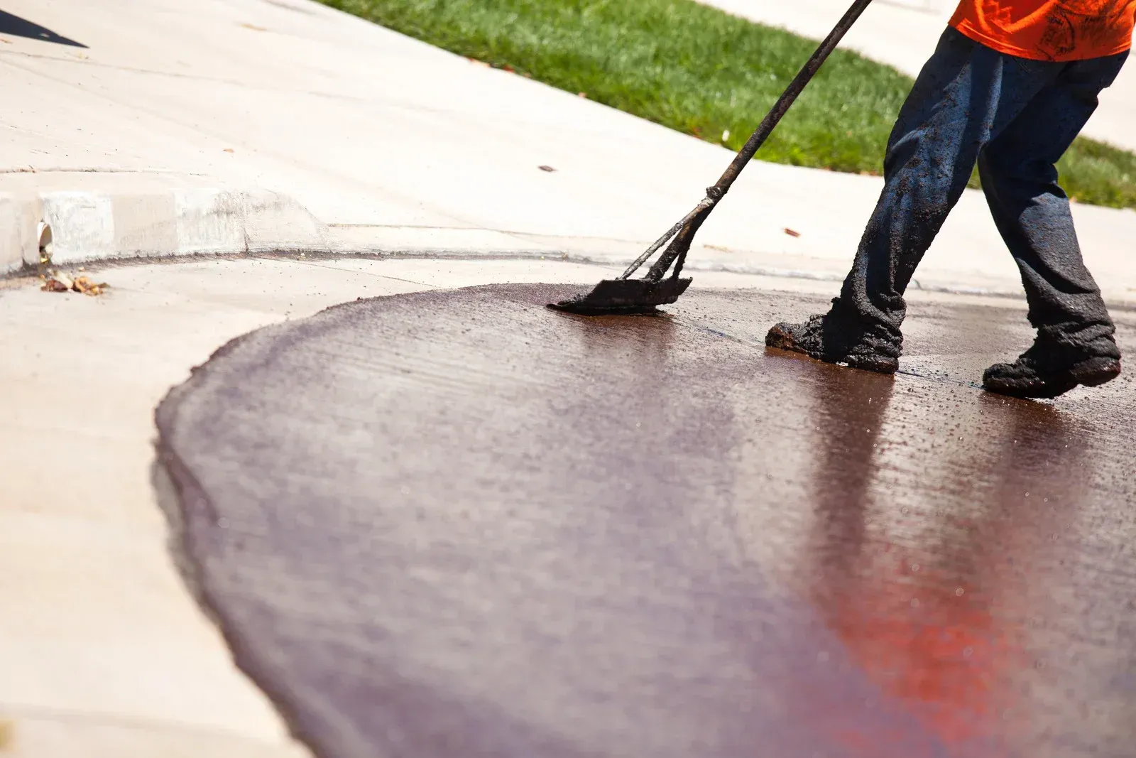 A person is spreading asphalt on a sidewalk with a broom.