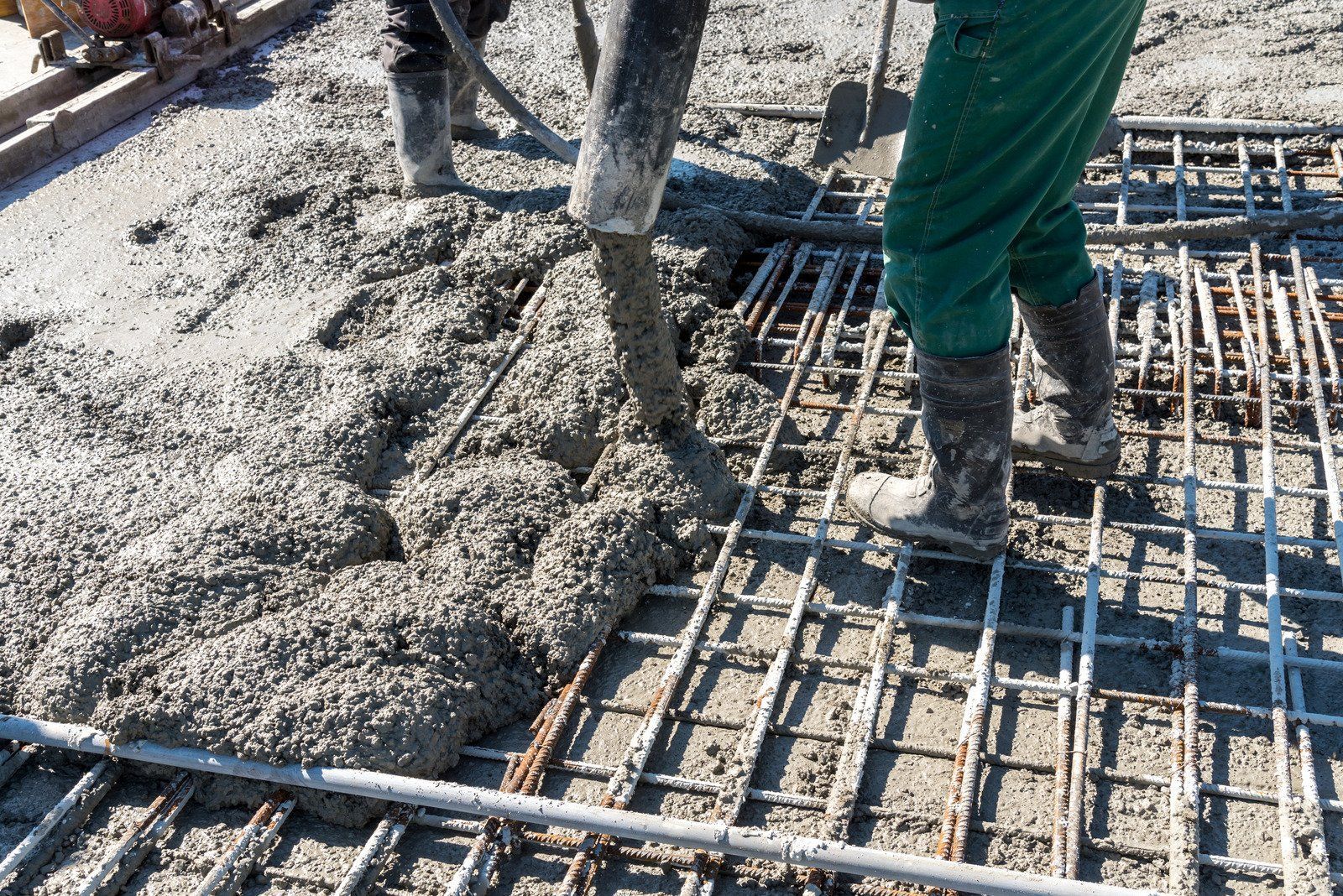 A man is pouring concrete into a metal grid on a construction site.