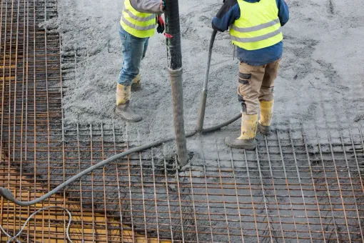 Two construction workers are pouring concrete into a grid.