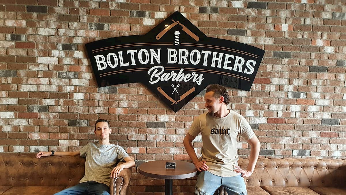 Two Men Posing Under Bolton Brothers Sign — Bolton Brothers Barbers in Erina, NSW