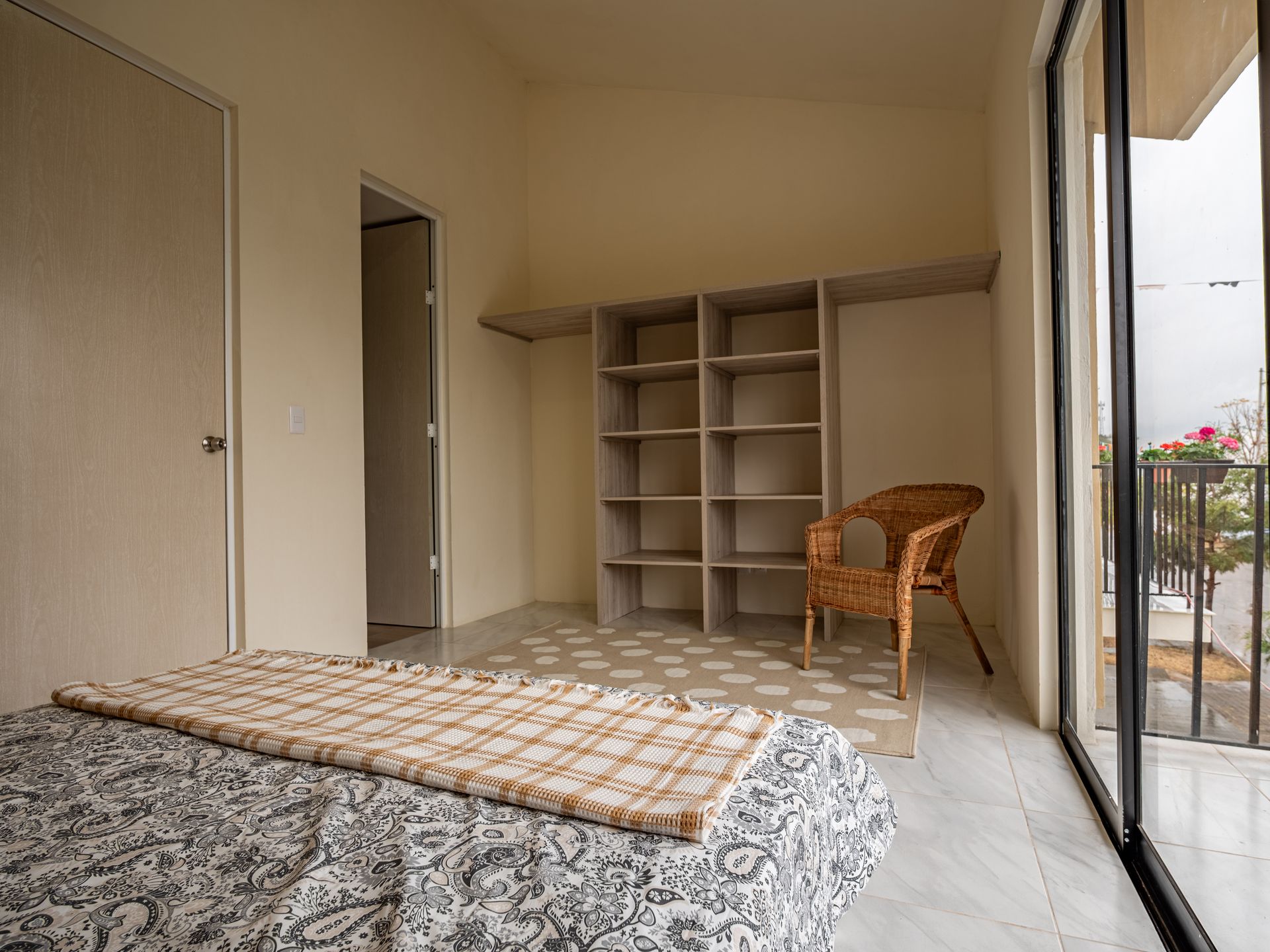 Un dormitorio con una cama, silla, estantes y una gran ventana.