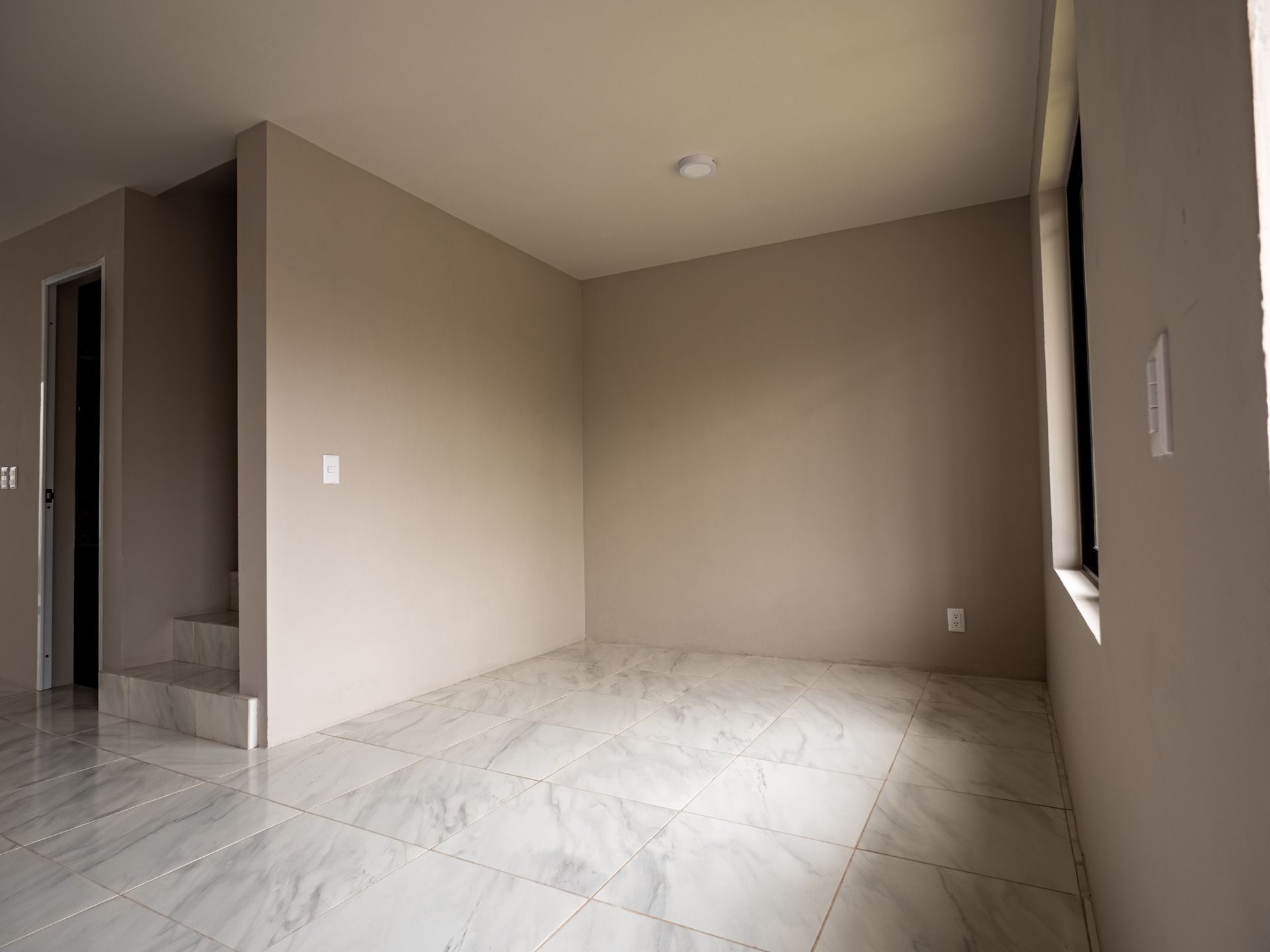 Una habitación vacía con pisos de mármol y paredes beige en una casa.