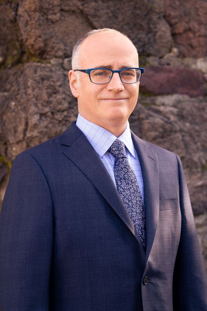 A man in a suit and tie is standing in front of a rock wall.