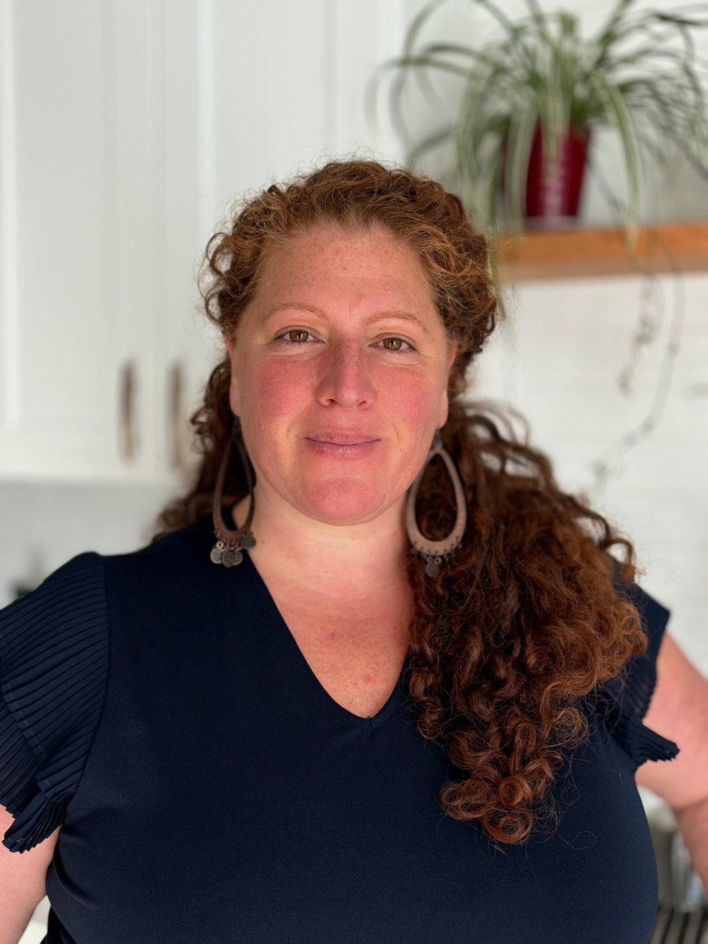 A woman with red hair is wearing a black shirt and earrings.