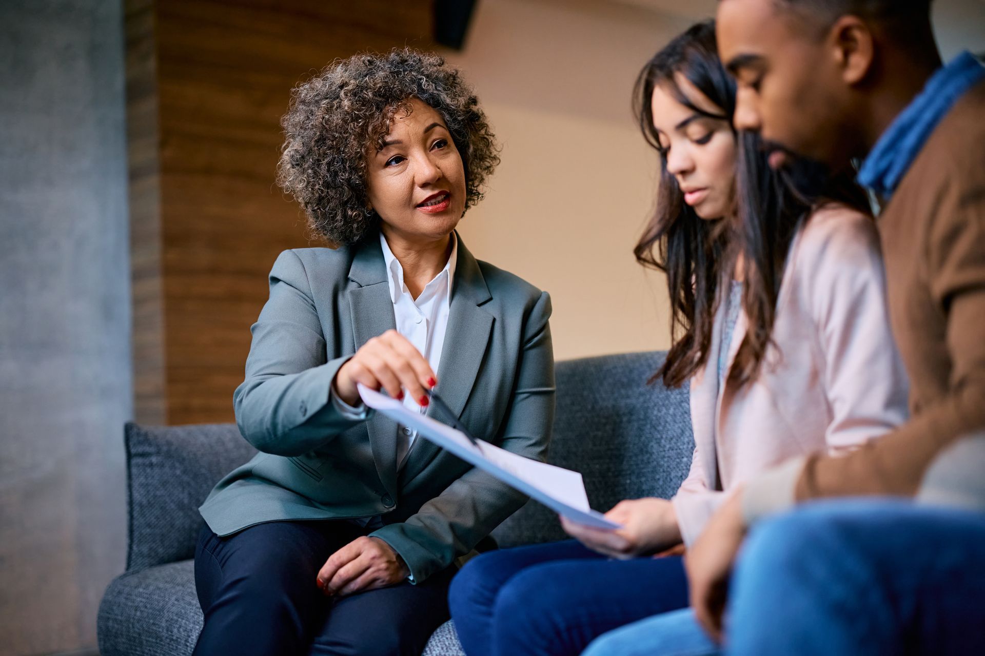 A woman is sitting on a couch talking to a man and a woman.