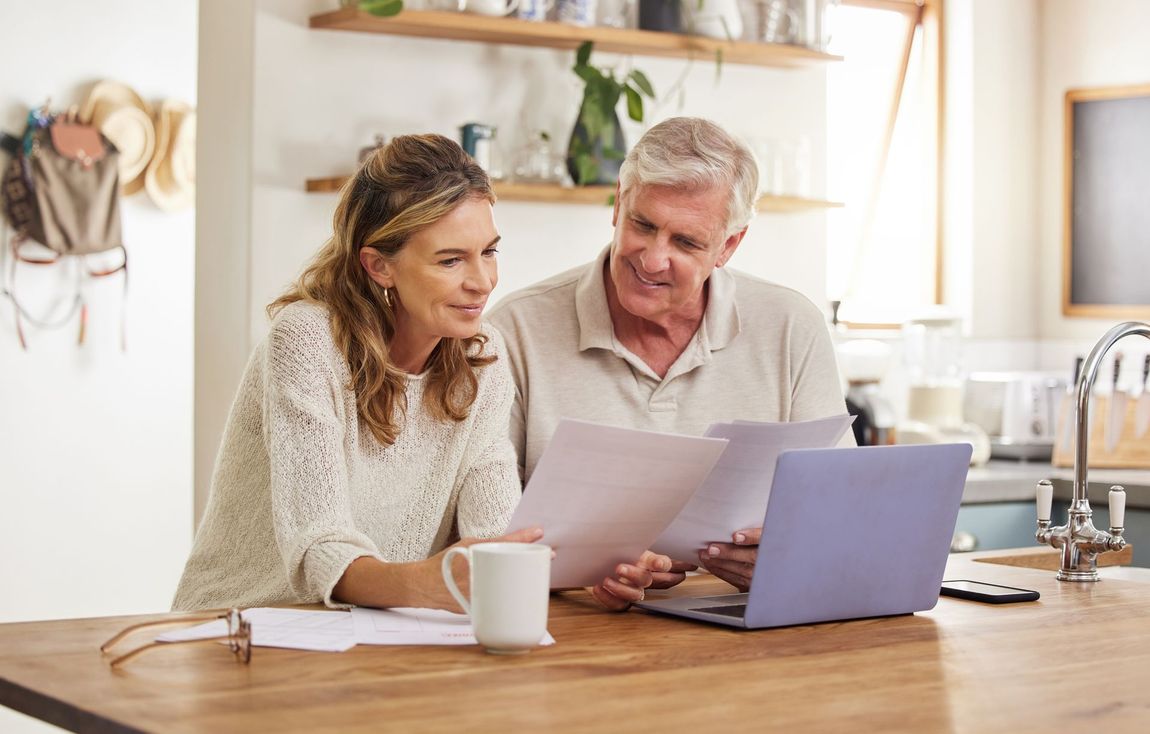 A man and woman are looking at a laptop computer in a kitchen.
