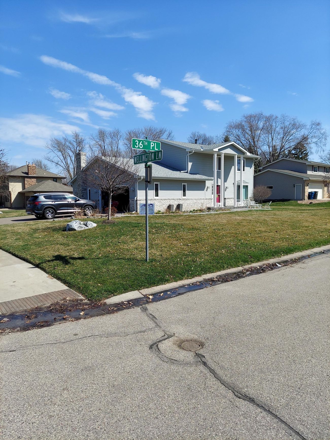 A house is sitting on a lush green lawn next to a street sign.