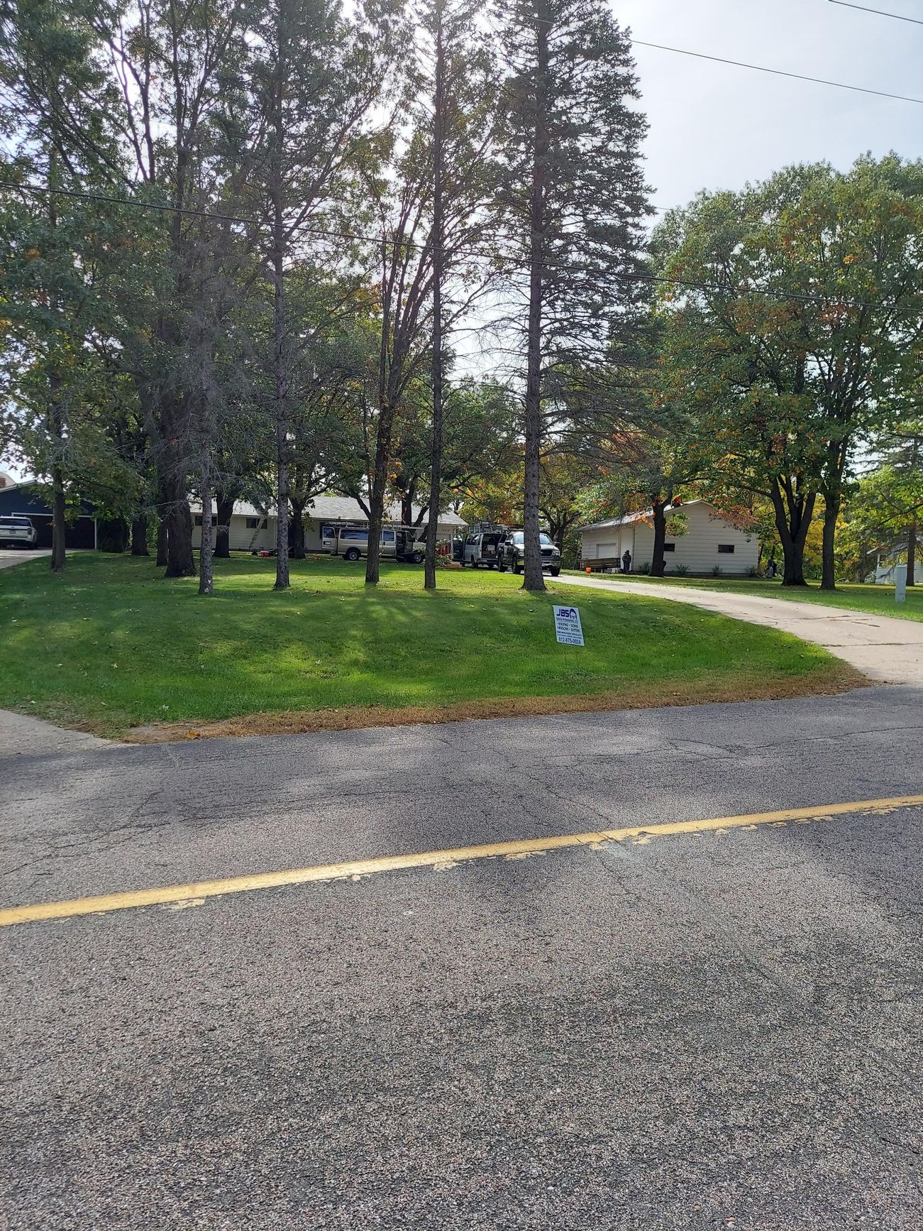 A gravel road leading to a grassy area with trees and a house in the background.