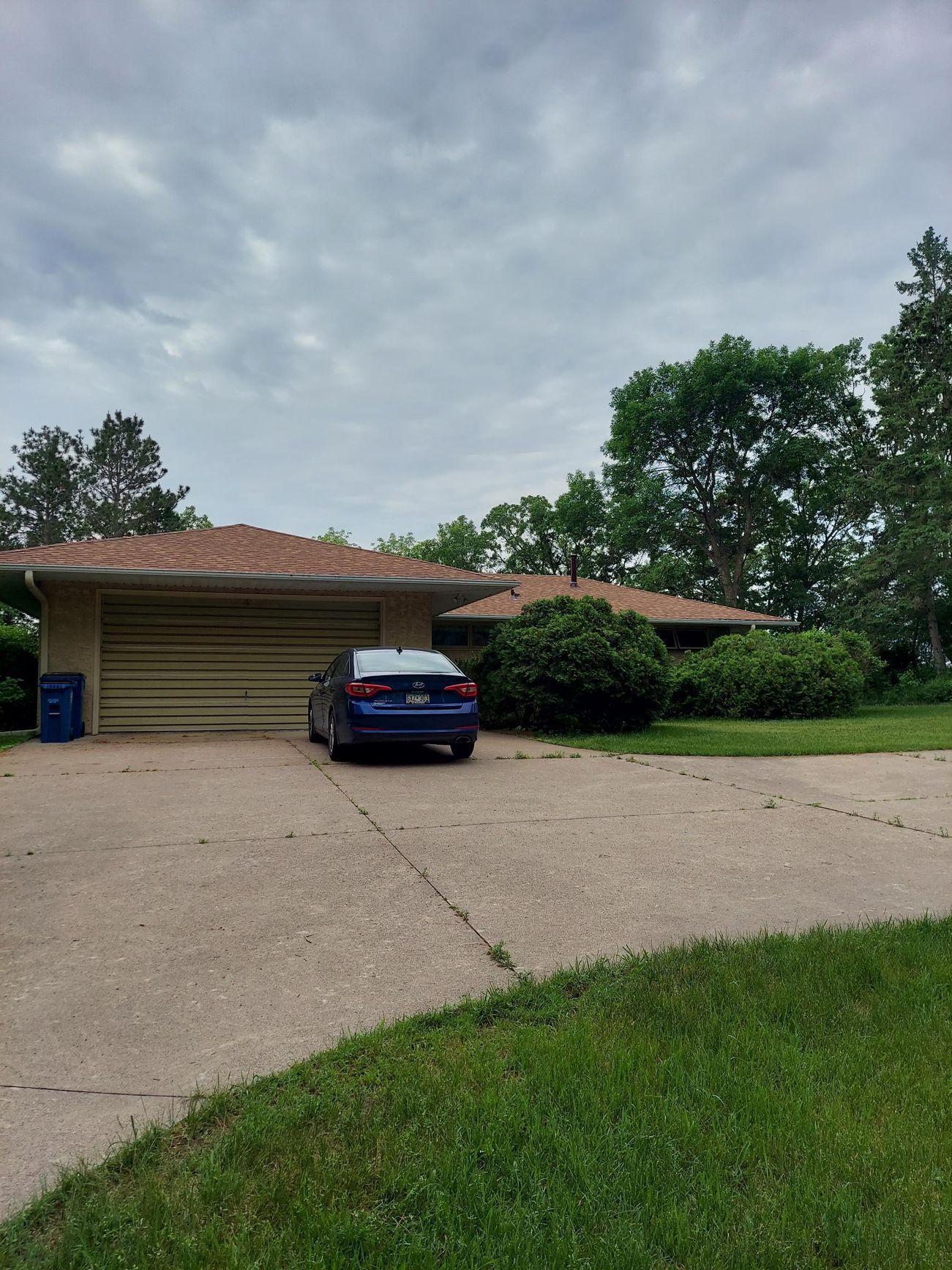 A blue car is parked in a driveway in front of a house.