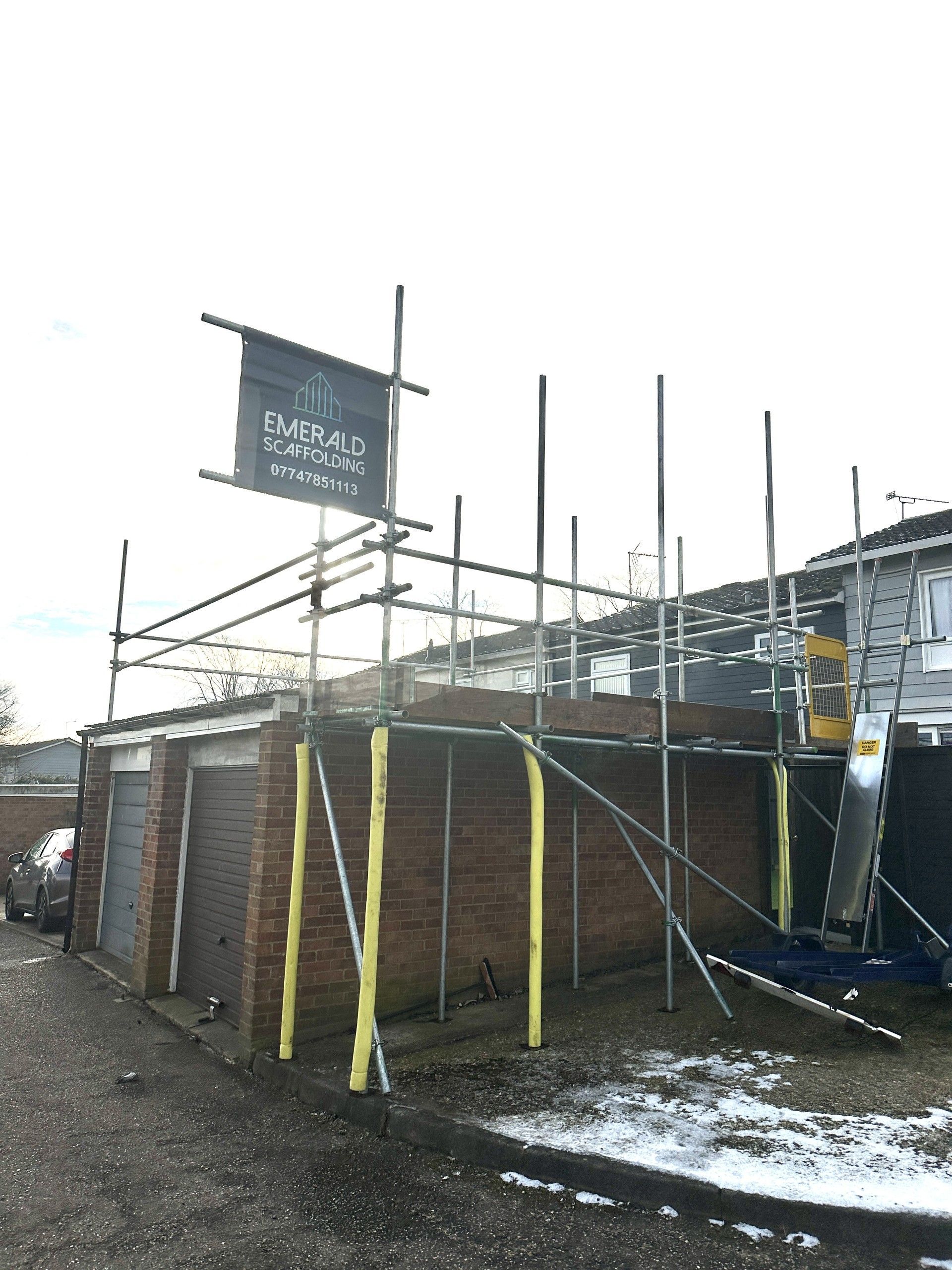 Scaffolding erected on a brick building with a business sign, snow on the ground.
