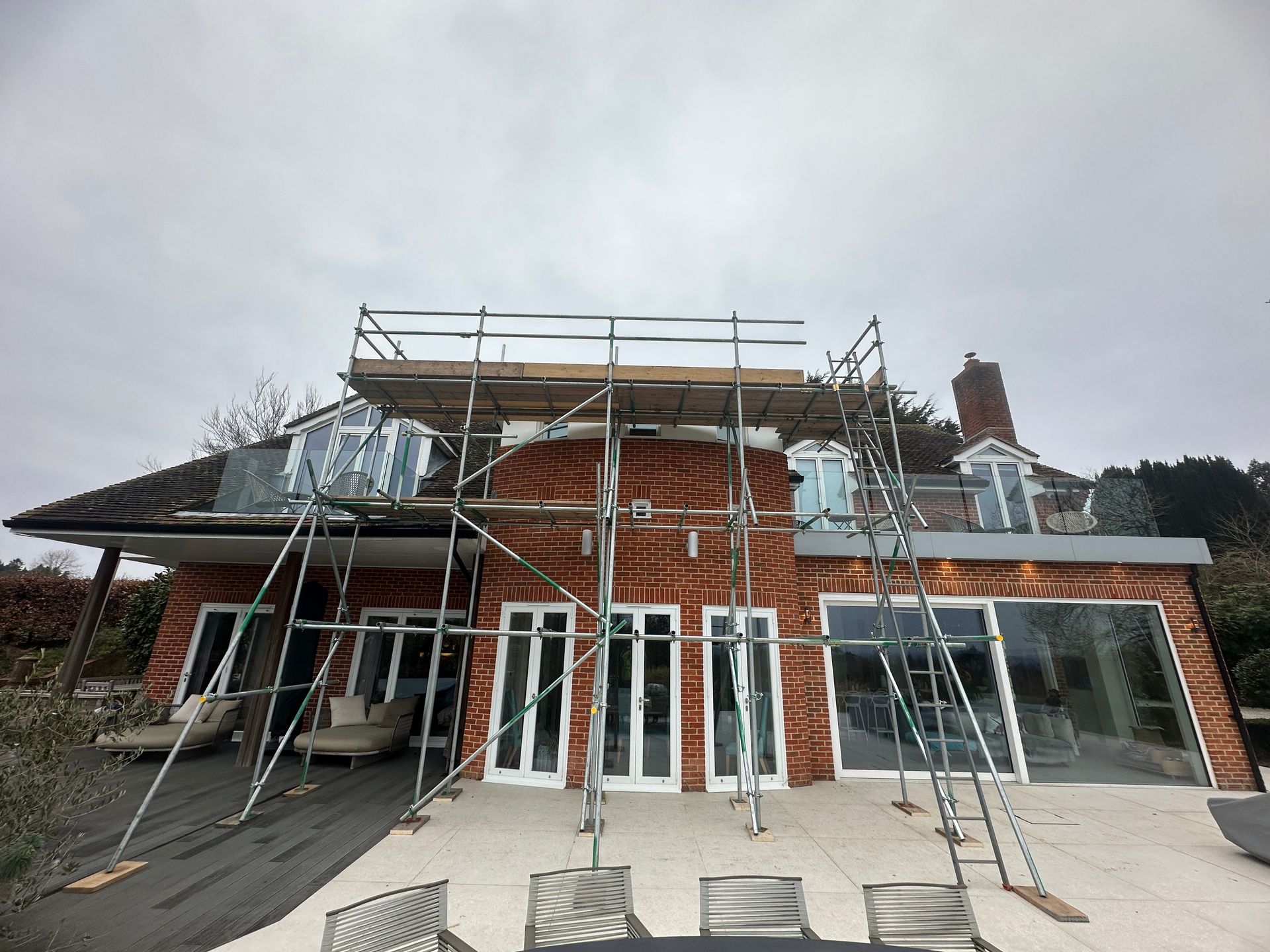 Scaffolding set up against a red brick house with glass windows and a cloudy sky.
