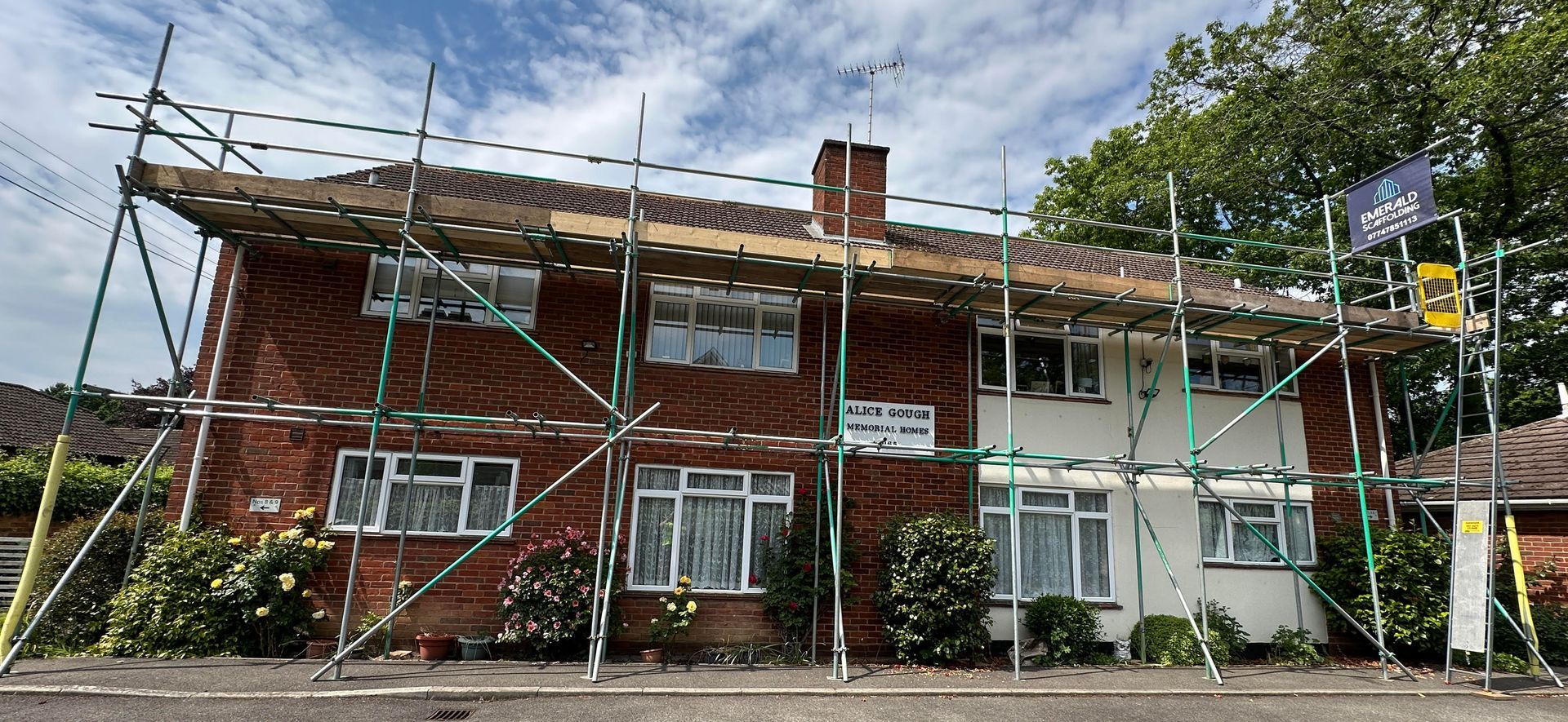 A two-story brick and white house with scaffolding. Roof repair in progress.