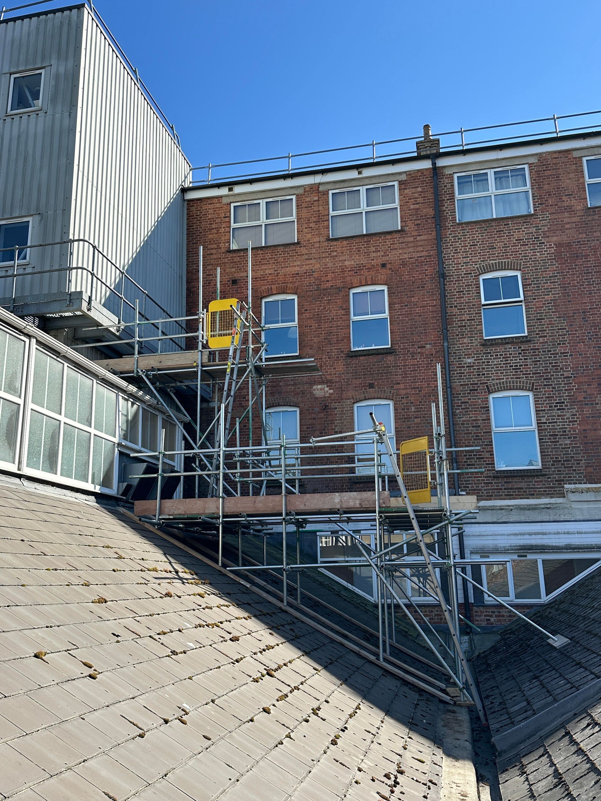 Scaffolding on a building with a red brick facade, blue sky.