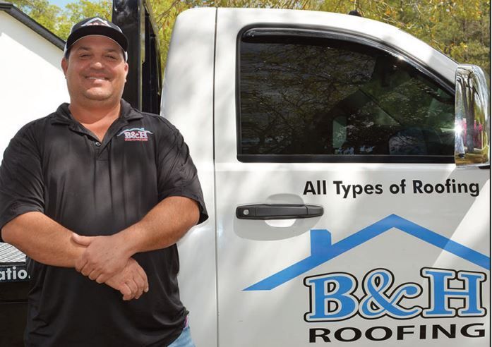 A man standing in front of a b & h roofing truck