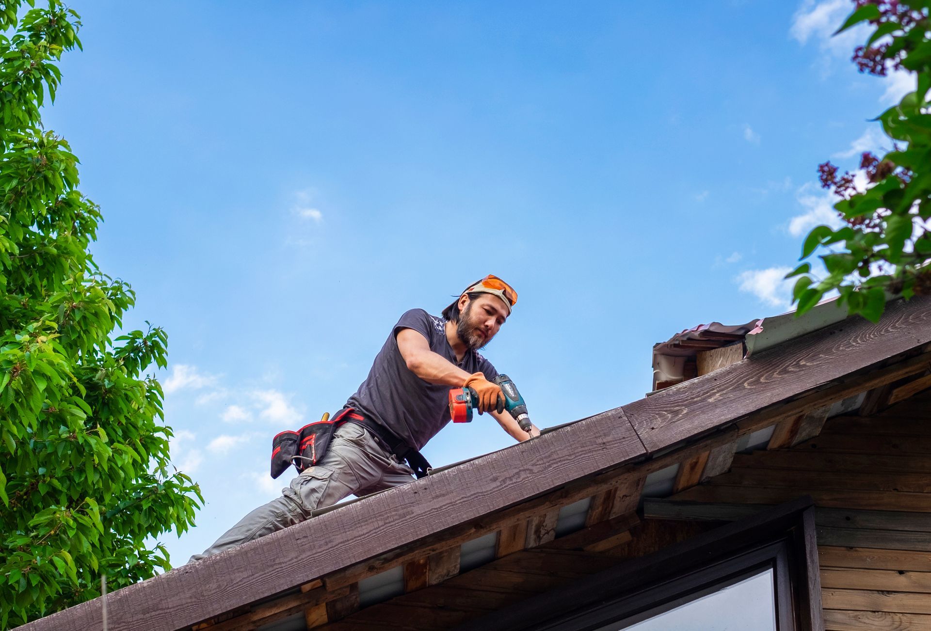 A worker performing roof repair on a house, by using an electric screwdriver.