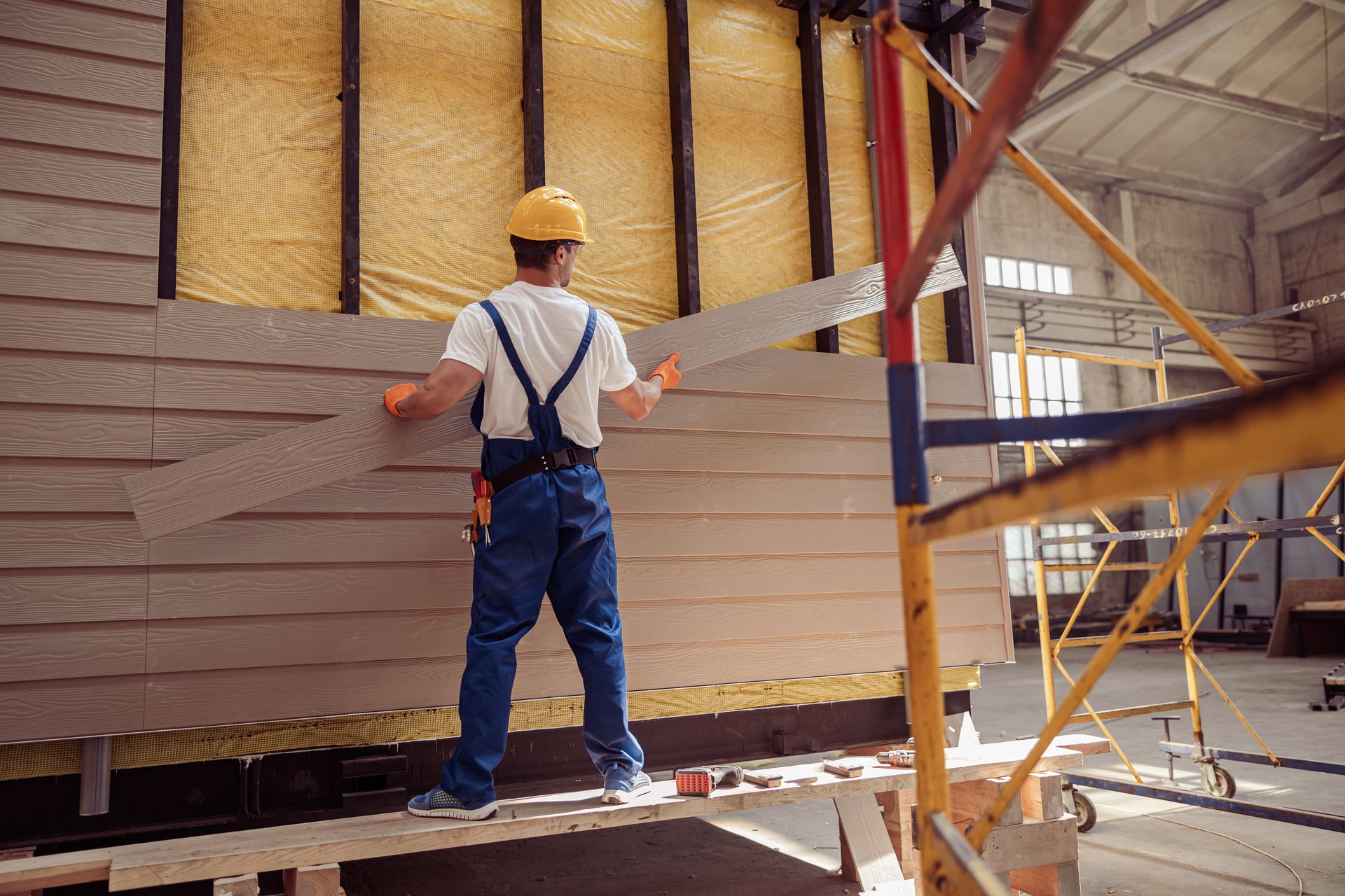 commercial siding contractor workers installing exterior panels on building gable using ladders.