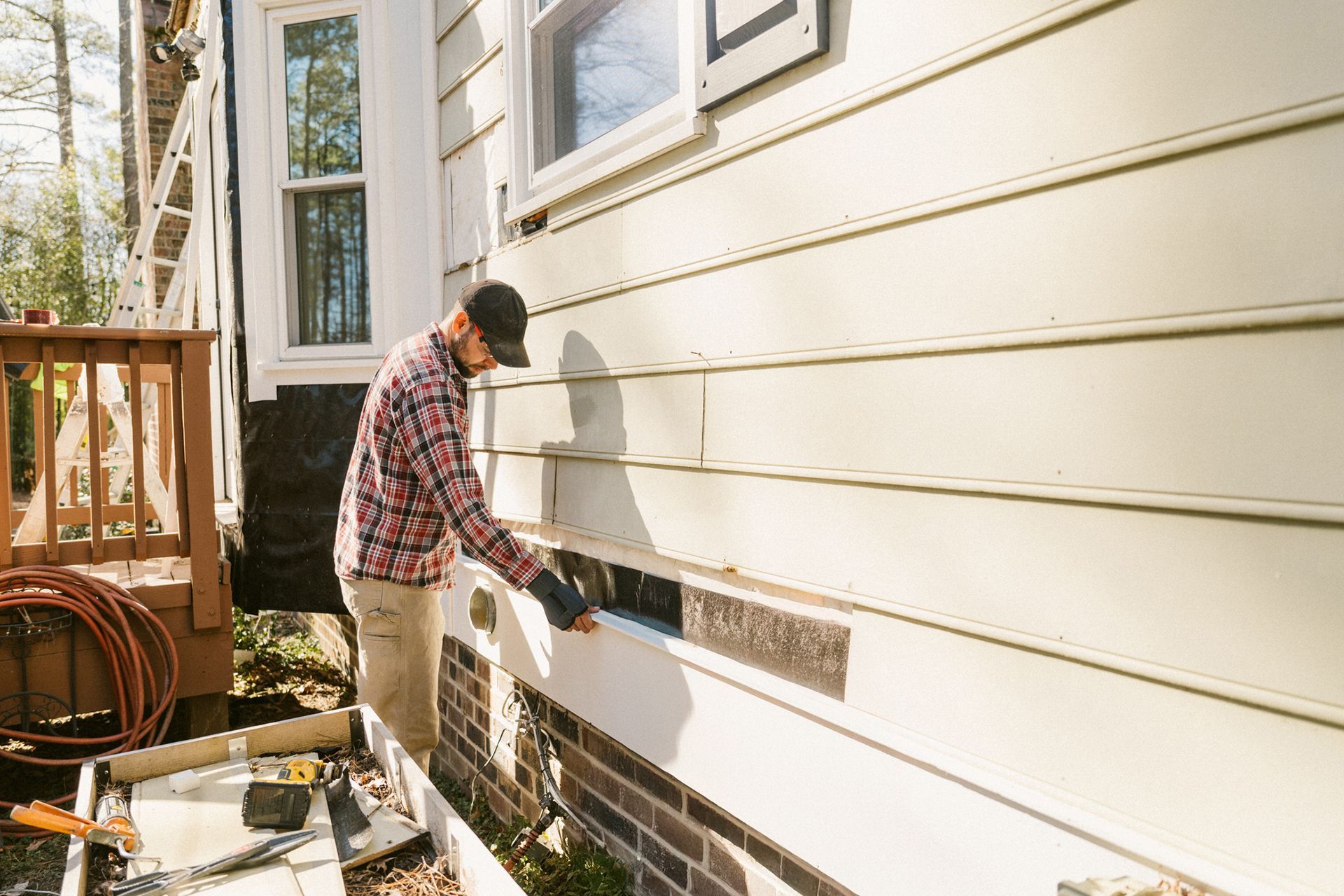 A man is working on residential siding installation, attaching panels to the exterior of a house. A man is working on residential siding installation, attaching panels to the exterior of a house.