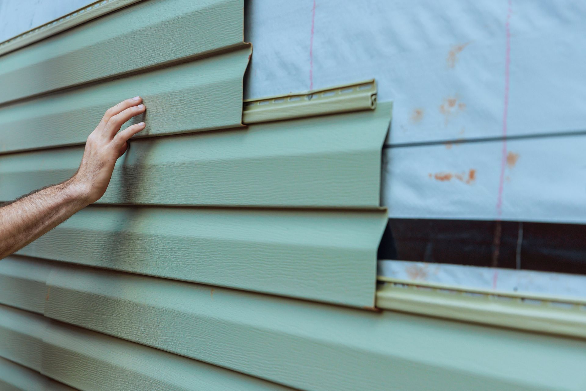 Close-up of vinyl siding being installed on a building exterior by a contractor.