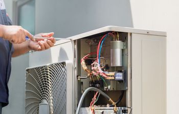 A technician uses a screwdriver to service the internal electrical components of an outdoor air conditioning unit.