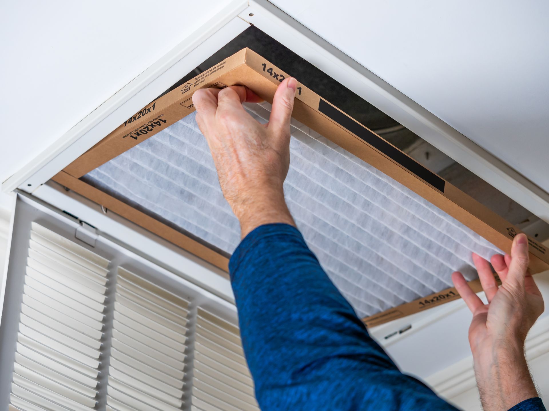 A person installs a rectangular air filter into a ceiling-mounted HVAC vent.