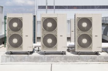 Three white industrial air conditioning units positioned side-by-side on a concrete rooftop.