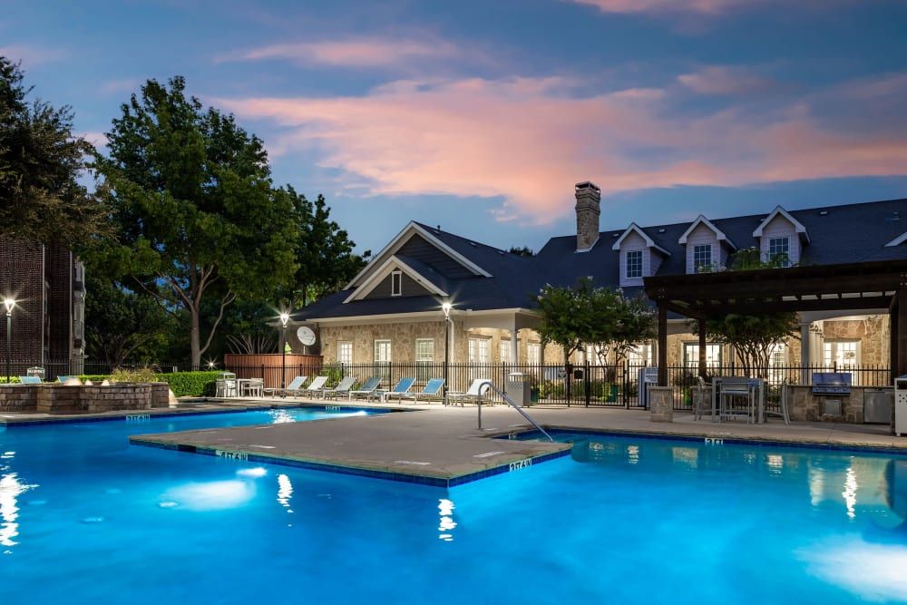 A large swimming pool in front of the clubhouse building at night at Marquis at Silver Oaks in Grapevine, TX.
