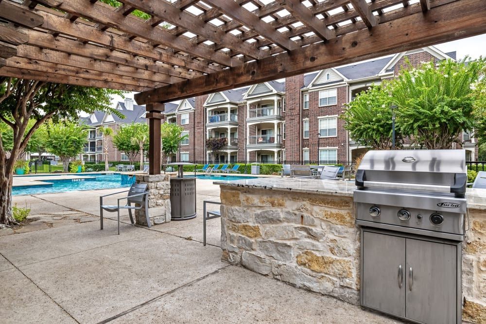 Outdoor grilling stations under a pergola next to a pool at Marquis at Silver Oaks in Grapevine, TX.