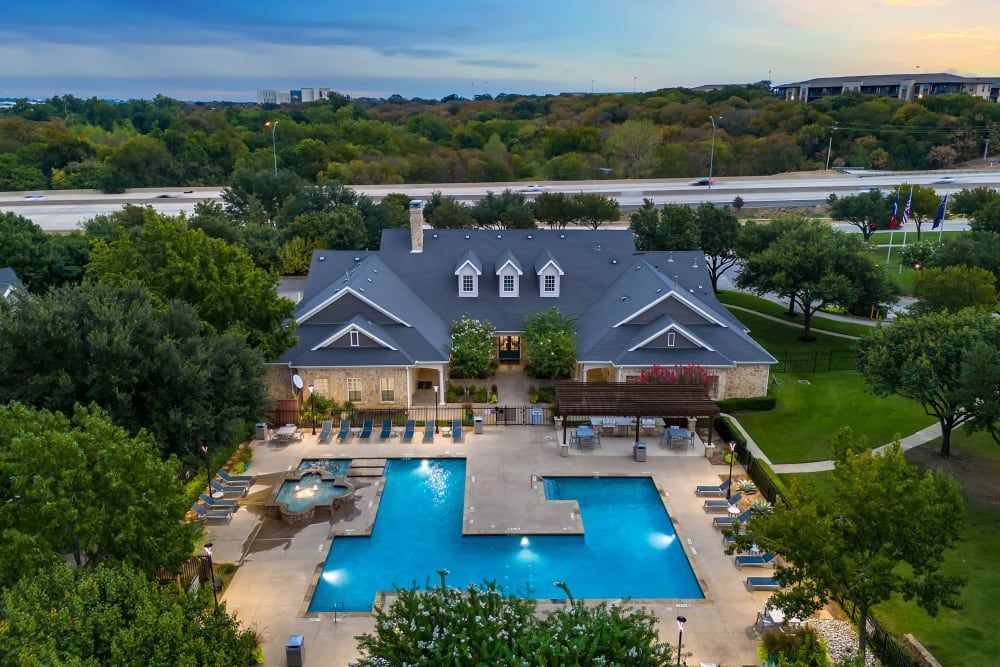 An aerial view of the outdoor swimming pool in front of the clubhouse surrounded by trees at Marquis at Silver Oaks in Grapevine, TX.