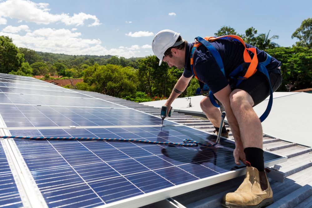 A Man Is Installing Solar Panels On The Roof Of A Building — Trusted Energy Solutions In Wilston, QLD