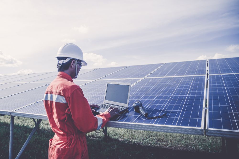 A Man Is Standing In Front Of A Solar Panel Using A Laptop — Trusted Energy Solutions In Coomera, QLD