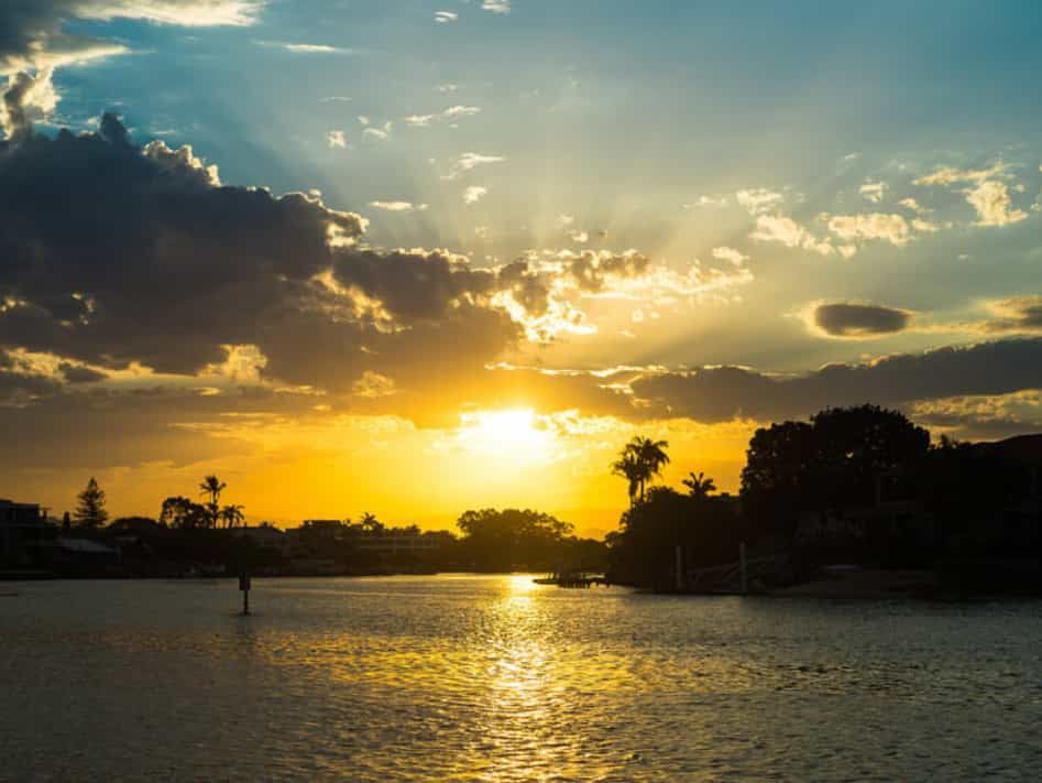 The Sun is Setting Over a Lake With Palm Trees in the Foreground — Trusted Energy Solutions In Nerang, QLD