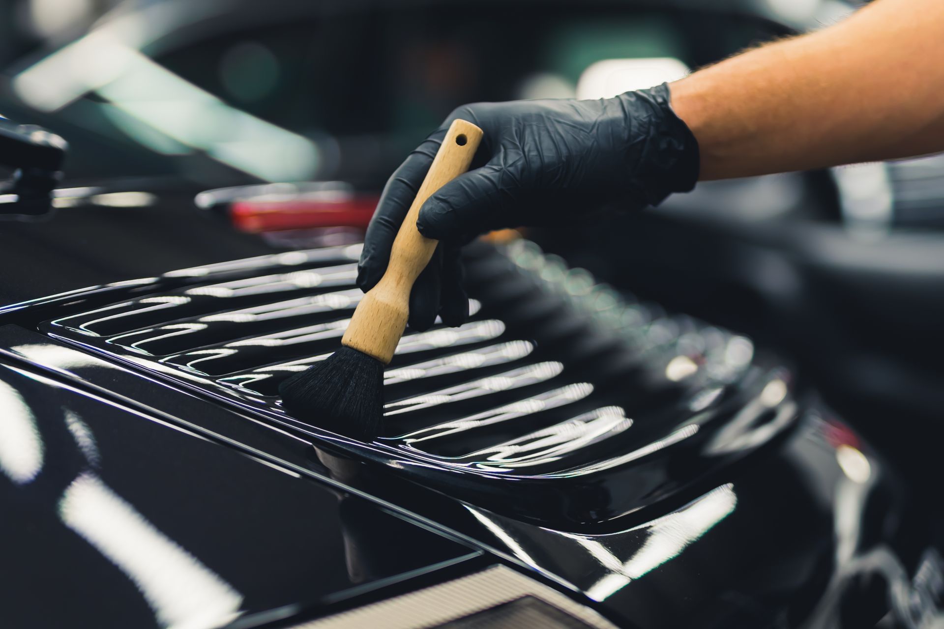 Luxurious sports car during car detailing. Unrecognizable man in protective gloves cleaning car spoiler with a brush.