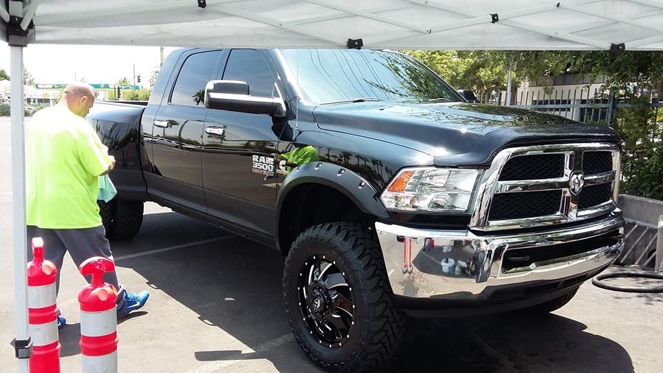 A man in a yellow shirt is standing next to a black truck.