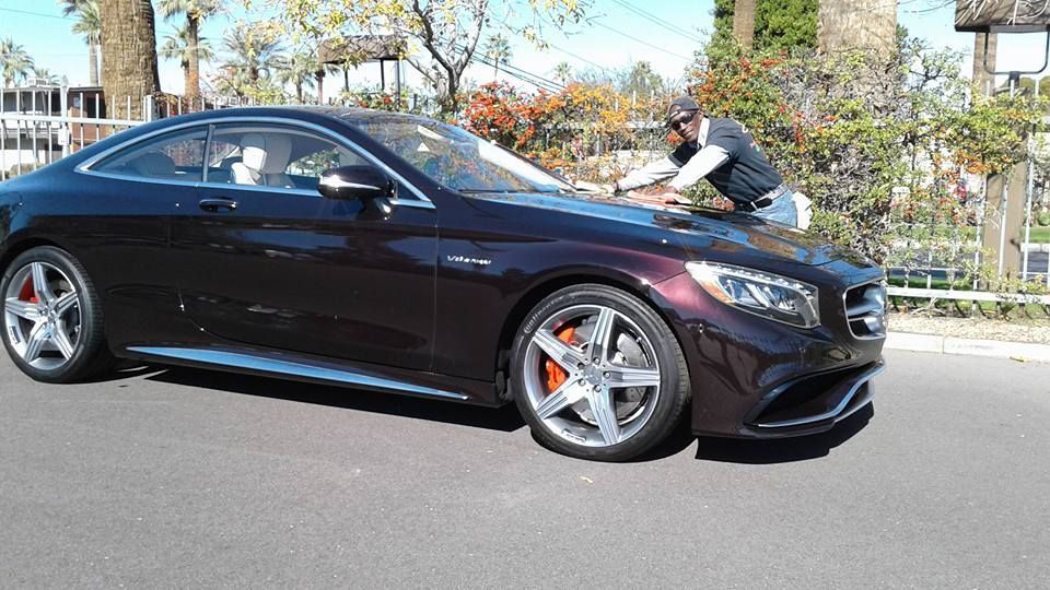 A man is cleaning the windshield of a mercedes benz s63 amg coupe.