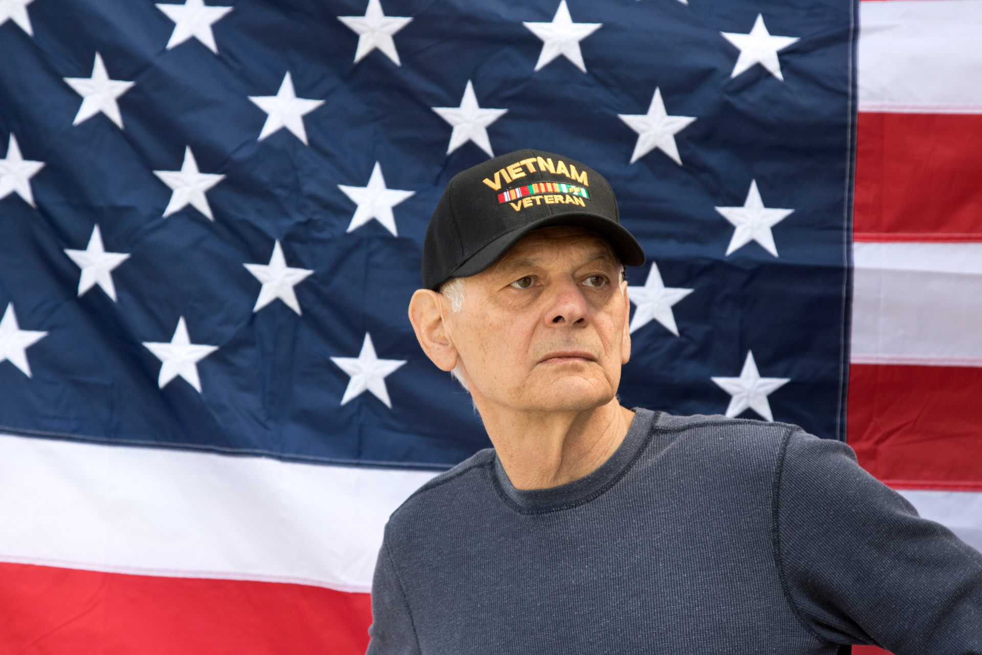 A man wearing a vietnam veteran hat is standing in front of an american flag.