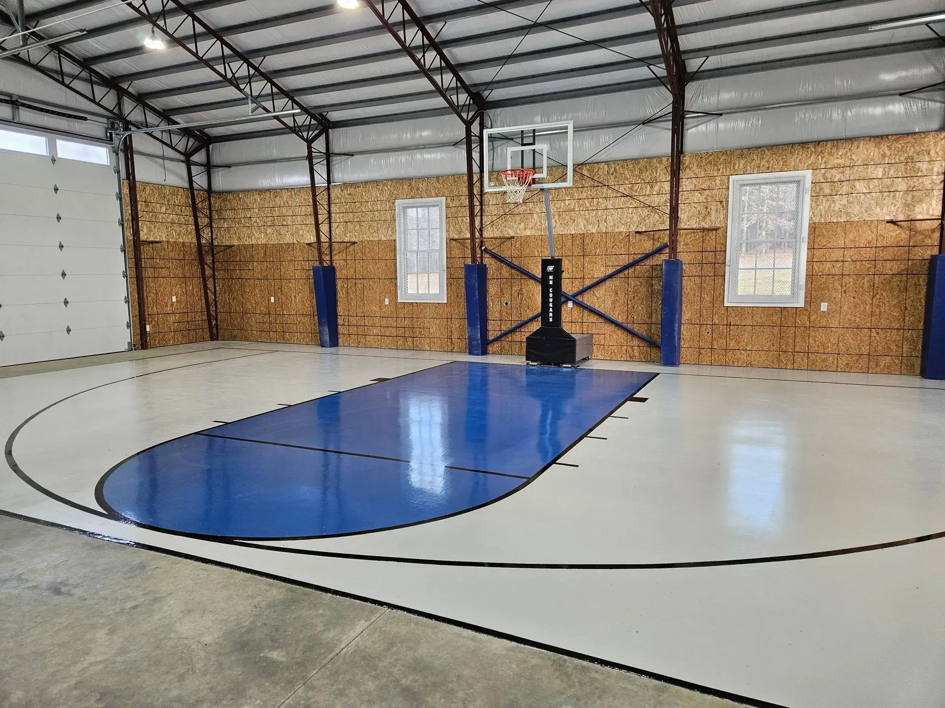 A blue and white basketball court in a garage with a basketball hoop.