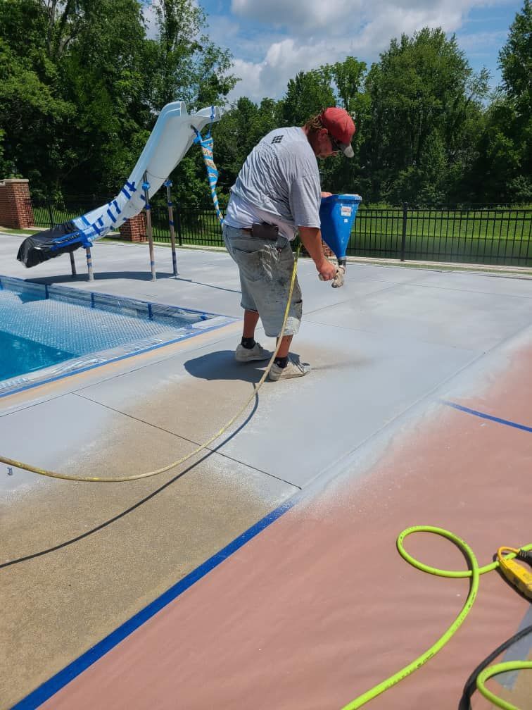 A man is painting a concrete deck next to a pool.