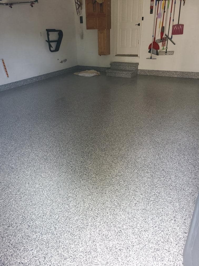 A garage with a gray floor and a bunch of tools on the wall.