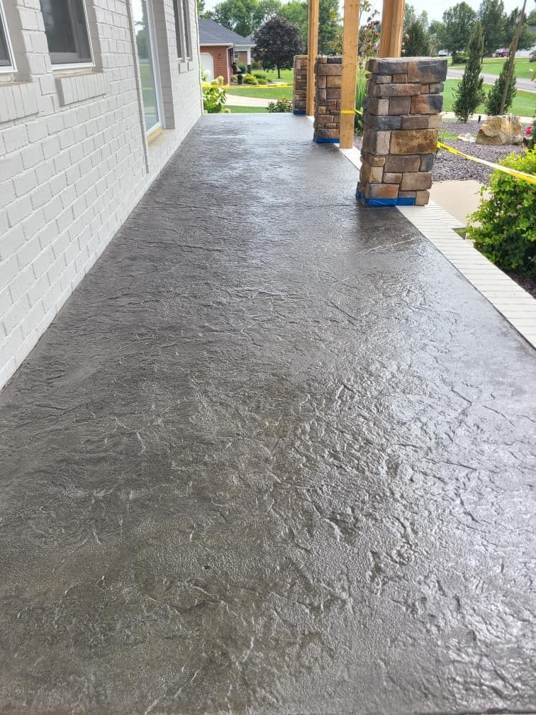 A concrete walkway leading to a house with brick pillars.
