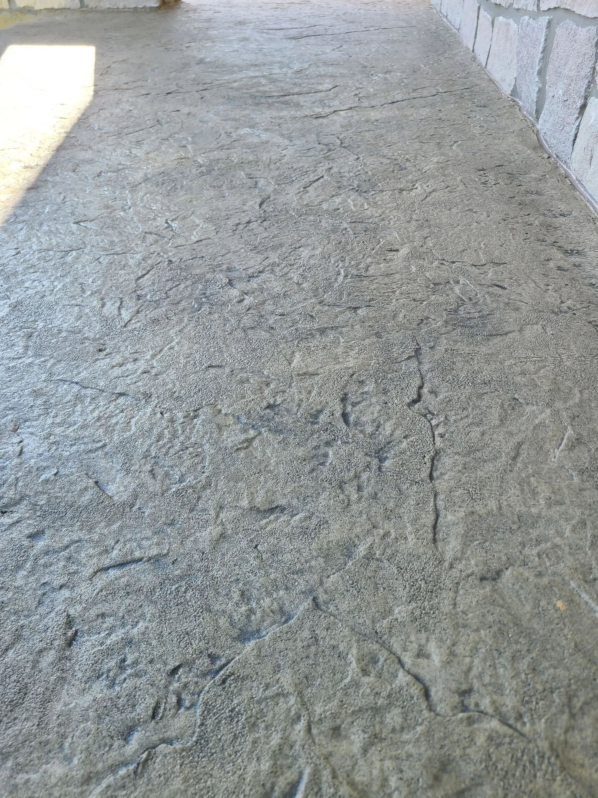 A close up of a concrete walkway with a stone wall in the background.