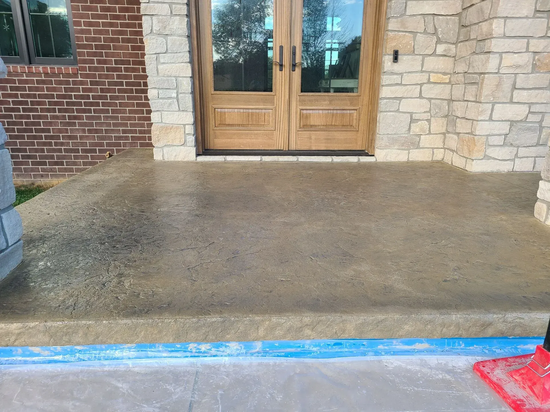 A concrete porch in front of a brick building with a wooden door.