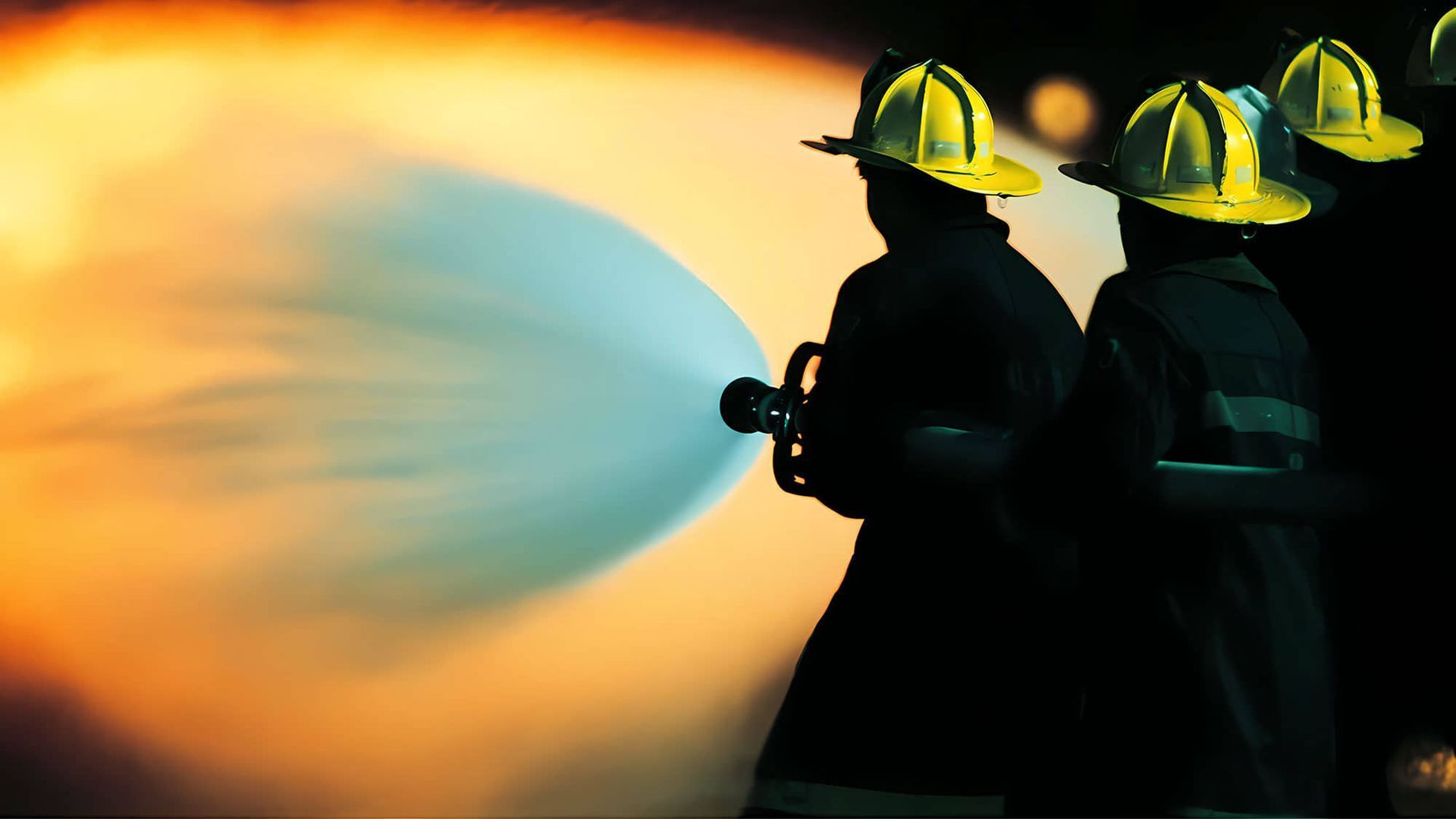 Bomberos, silueteados, rociando agua con una manguera; un resplandor naranja ilumina el agua y el entorno.