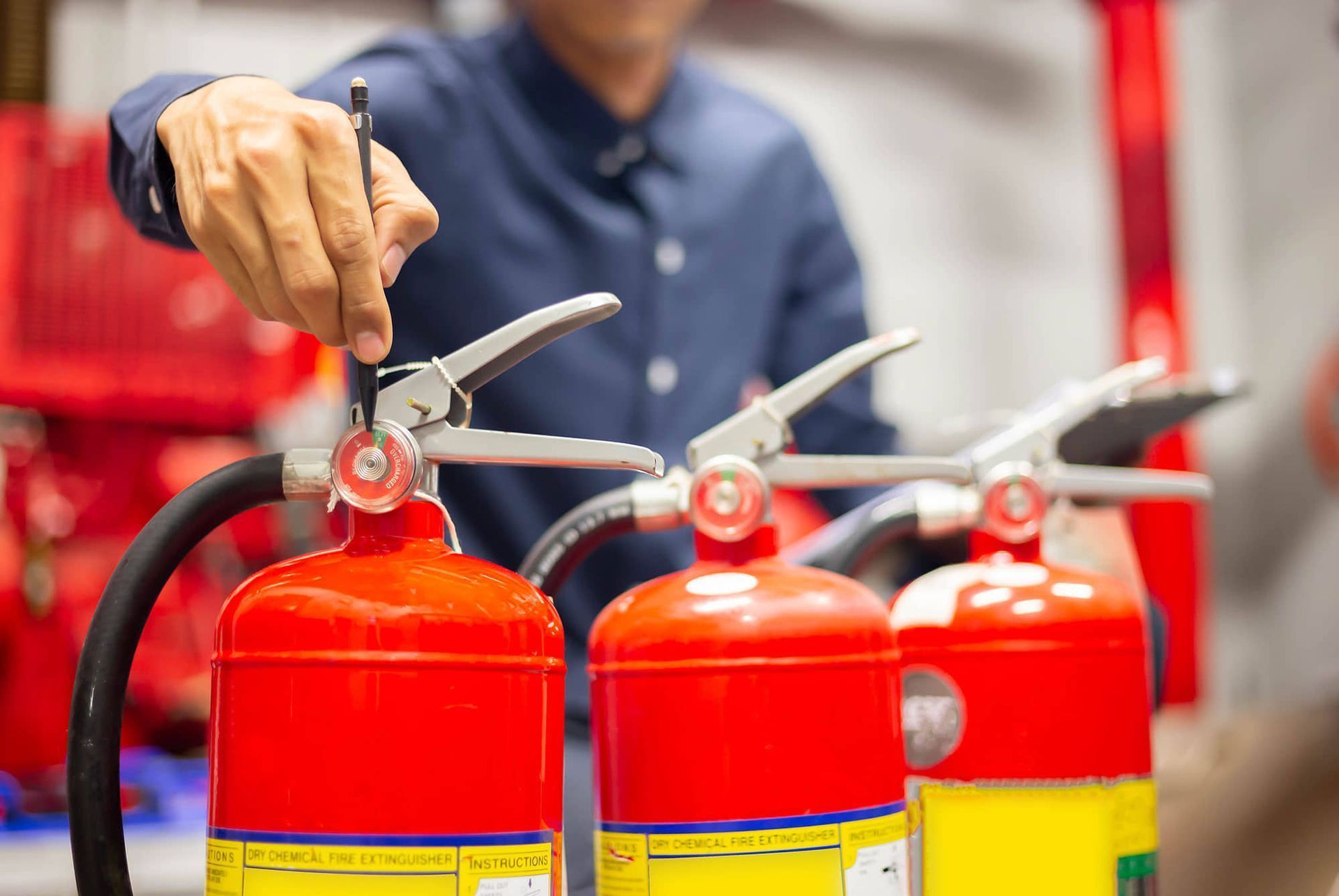 Persona inspeccionando extintores; tanques rojos, enfocado en controles de seguridad.
