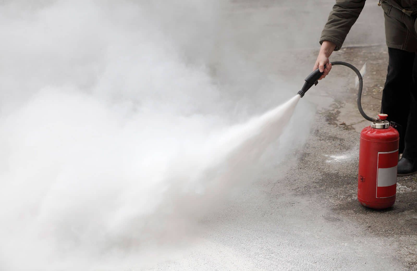 Persona rociando una sustancia blanca desde un extintor rojo sobre una superficie de concreto.