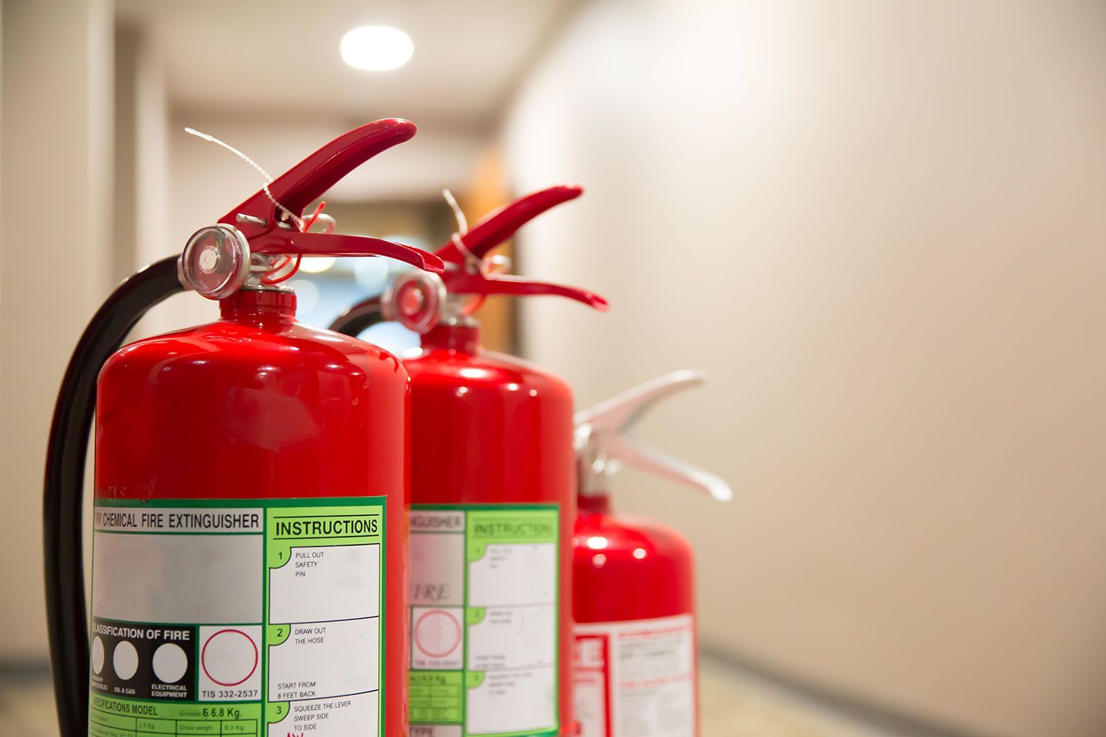 Tres extintores rojos alineados en un pasillo.